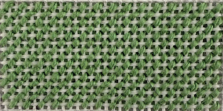 Skipped Tent, one of the small-scale needlepoint stitches, worked in green thread on white canvas.