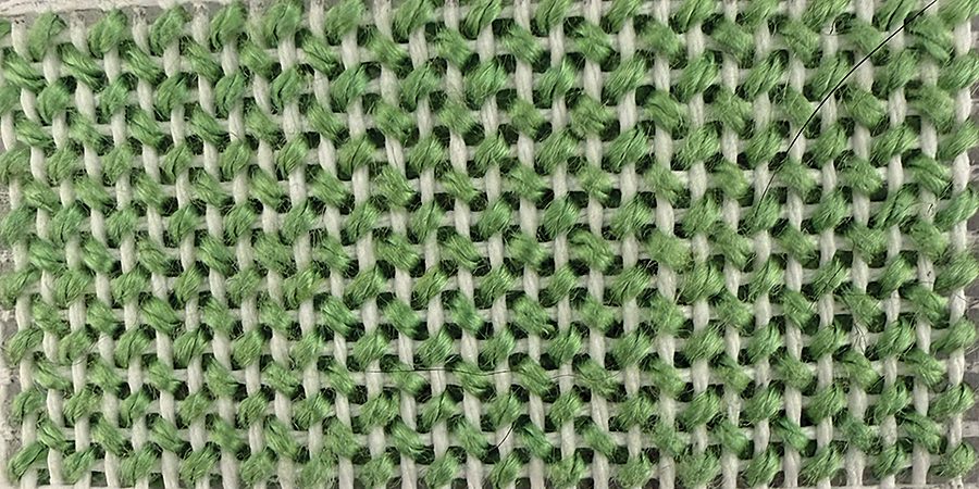 T-Stitch in green thread on white canvas, a small needlepoint background stitch that suits narrow and tightly curved areas.