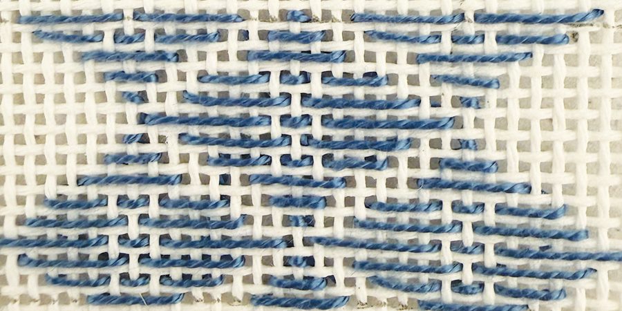 Wide Diamond, one of the large-scale needlepoint stitches, worked in blue thread on white canvas.